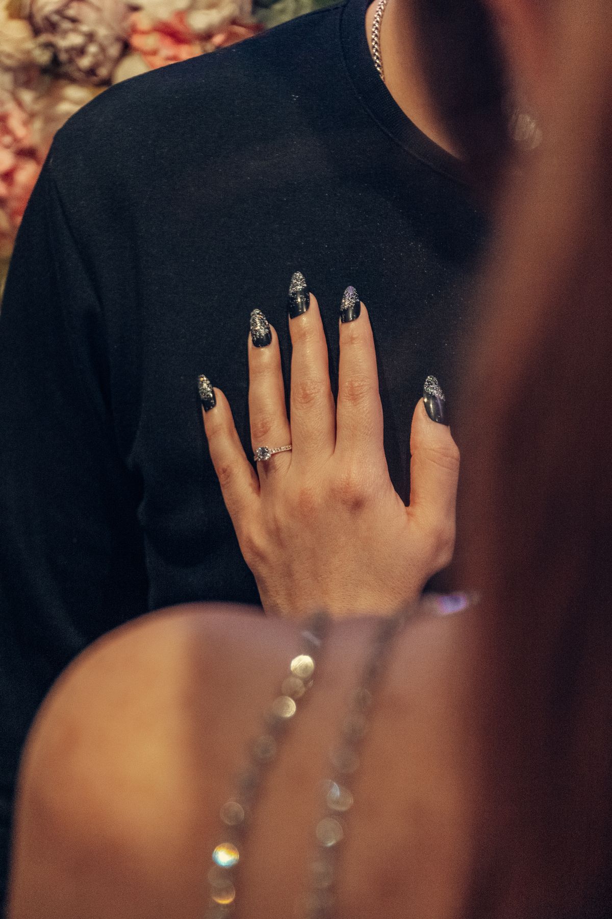 Elegant woman's hand with glitter nail art and ring touching a man's chest in a close portrait.