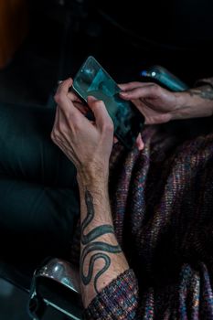 A person with a snake tattoo on their arm using a smartphone.