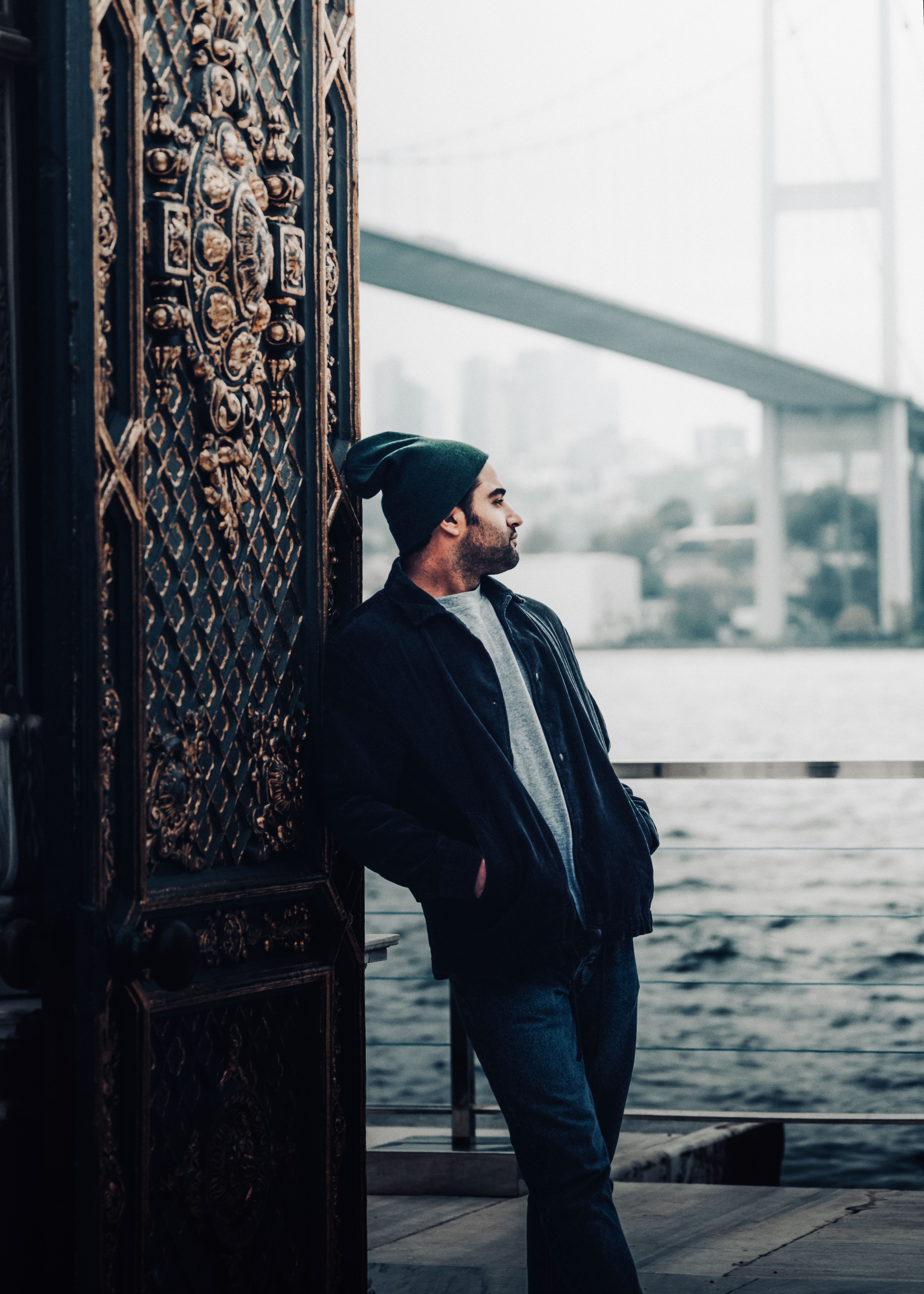 Man Standing and Leaning against the Door with a Bridge and Sea in the ...