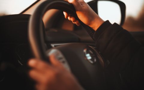 Hands on a steering wheel in warm golden light during a careful drive