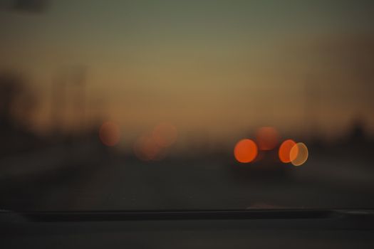 Blurry abstract image of car lights with warm tones at dusk, creating a bokeh effect.