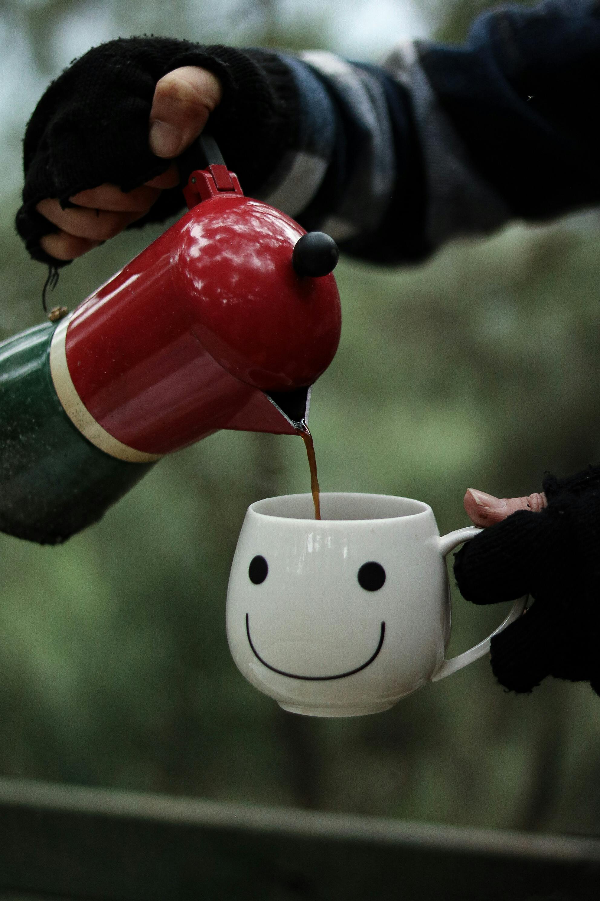 Hands pouring coffee into a smiley face mug, creating a warm and cozy atmosphere.