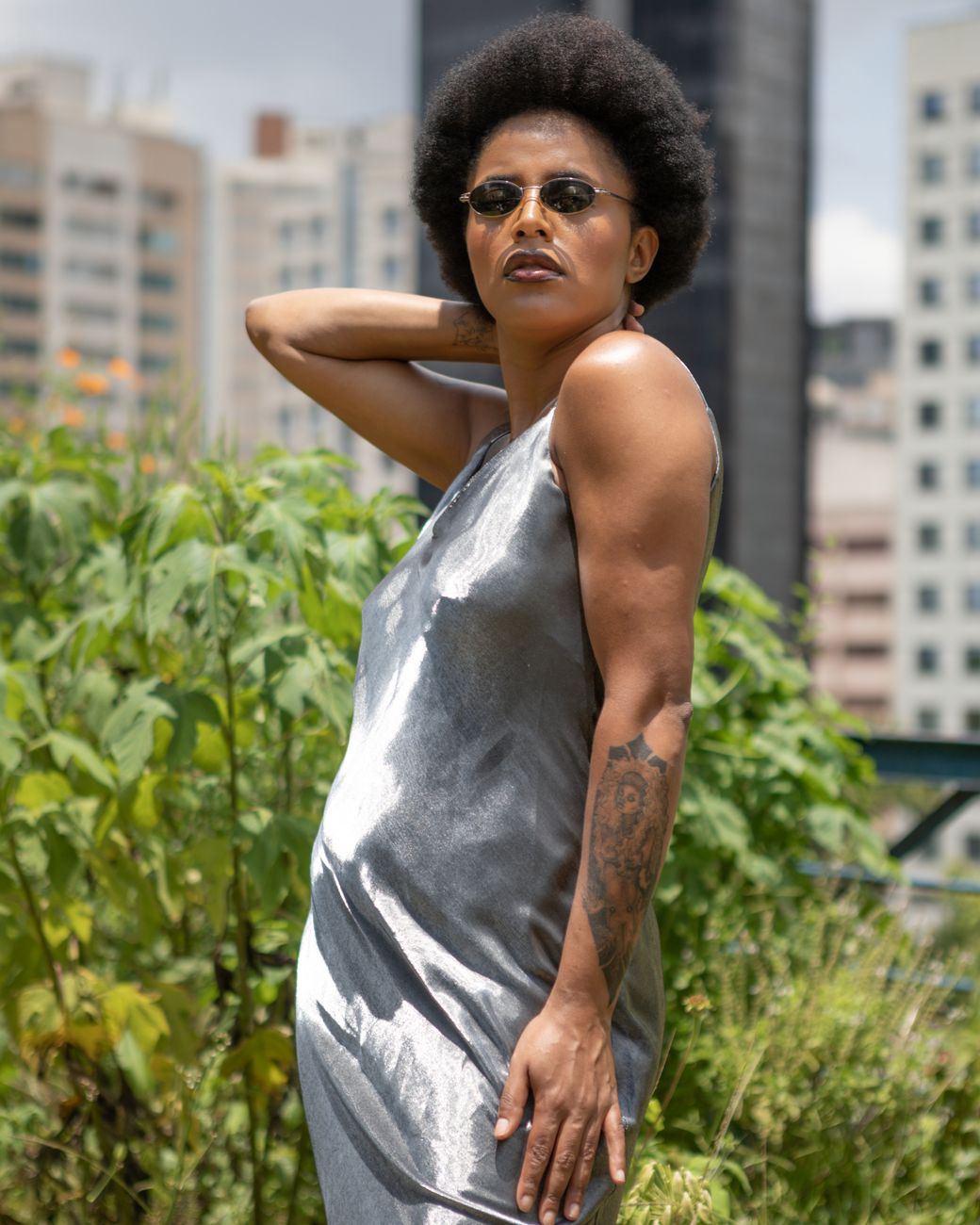 Mulher confiante em um vestido prateado com óculos de sol posando em um ambiente urbano.