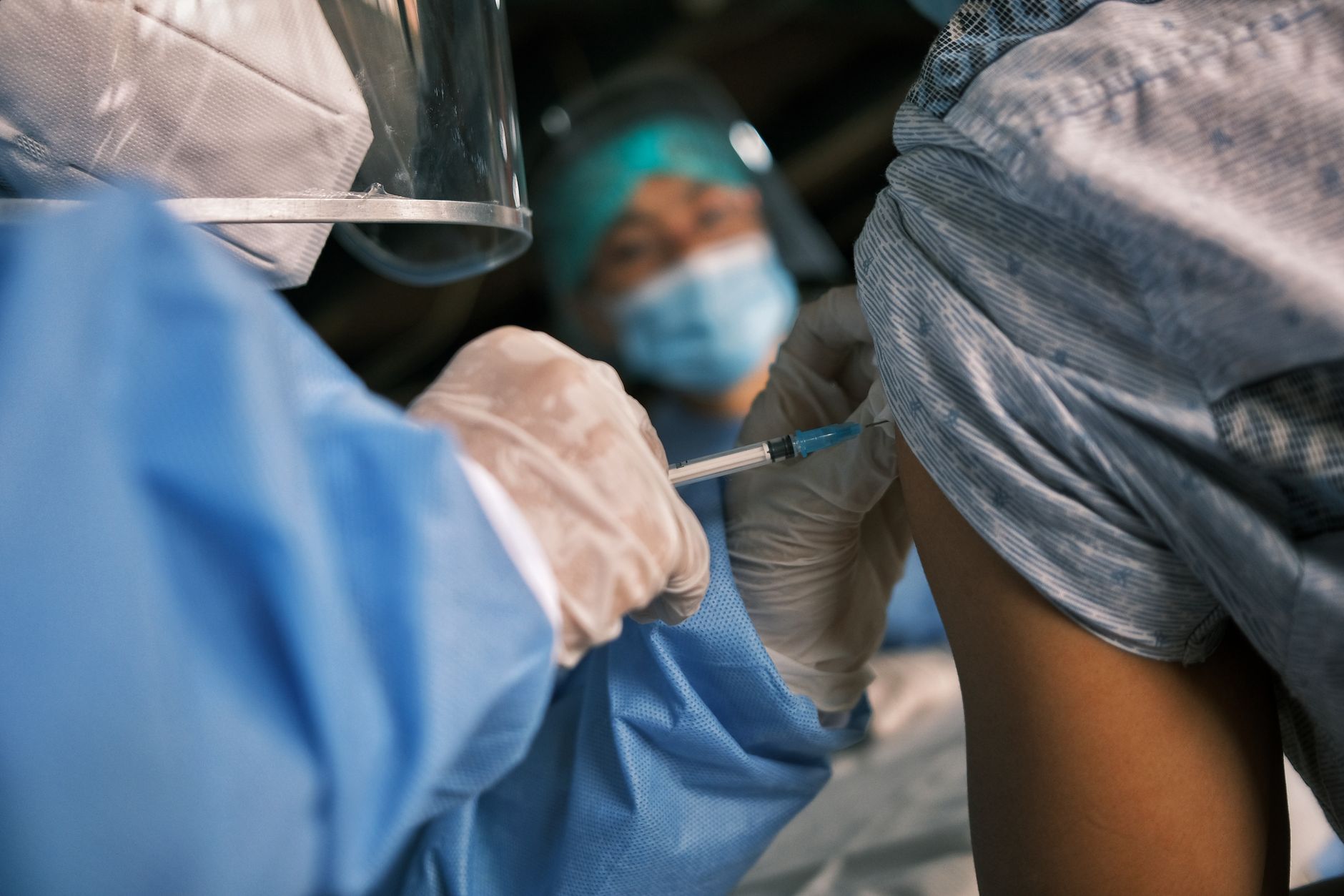 Healthcare professional wearing protective gear giving a vaccination to a patient.