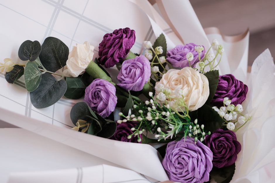 A close-up shot of a beautifully arranged artificial flower bouquet with white and purple roses.
