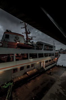 A cruise ship moored at a harbor under an overcast sky at dusk, creating a moody atmosphere.