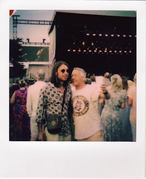 Two men posing at a lively outdoor music festival under a sunny day.