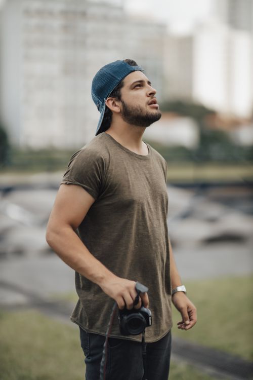 Free Candid shot of a young male photographer in a park, holding a camera. Stock Photo