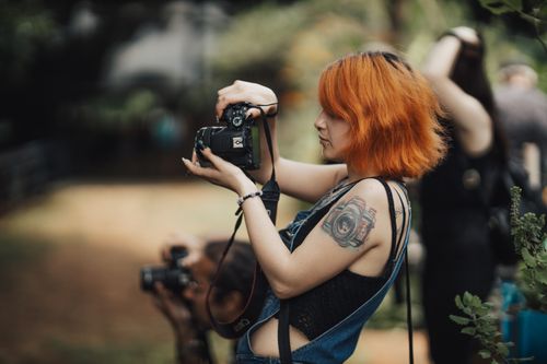 Free Red-haired woman with tattoos captures nature moments outdoors with a professional camera. Stock Photo