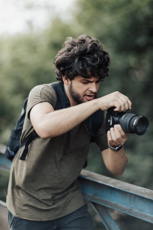 Free A male photographer using a DSLR camera outdoors, focusing intently on his shot. Stock Photo
