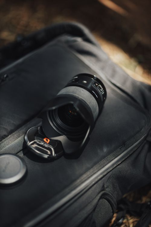 Free A detailed shot of a camera lens placed on a backpack outdoors, ideal for photography and travel themes. Stock Photo