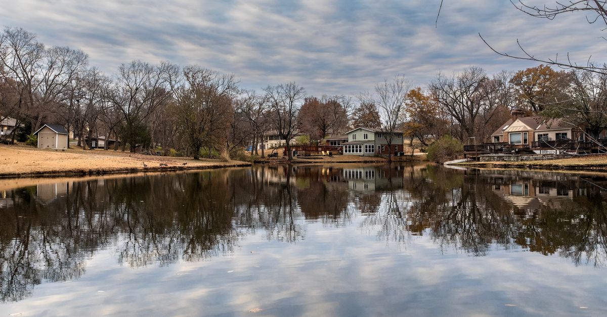 Peaceful autumn scene of lakeside homes reflecting on tranquil water in Platte Woods.