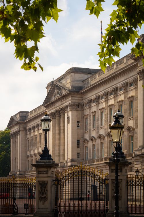 Free Majestic view of Buckingham Palace, a famous landmark in London, surrounded by ornate gates and lush greenery. Stock Photo