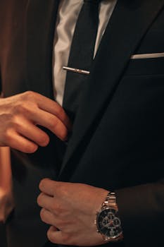 Close-up of a man in a suit adjusting his tie and showcasing a stylish wristwatch, capturing sophistication and style.