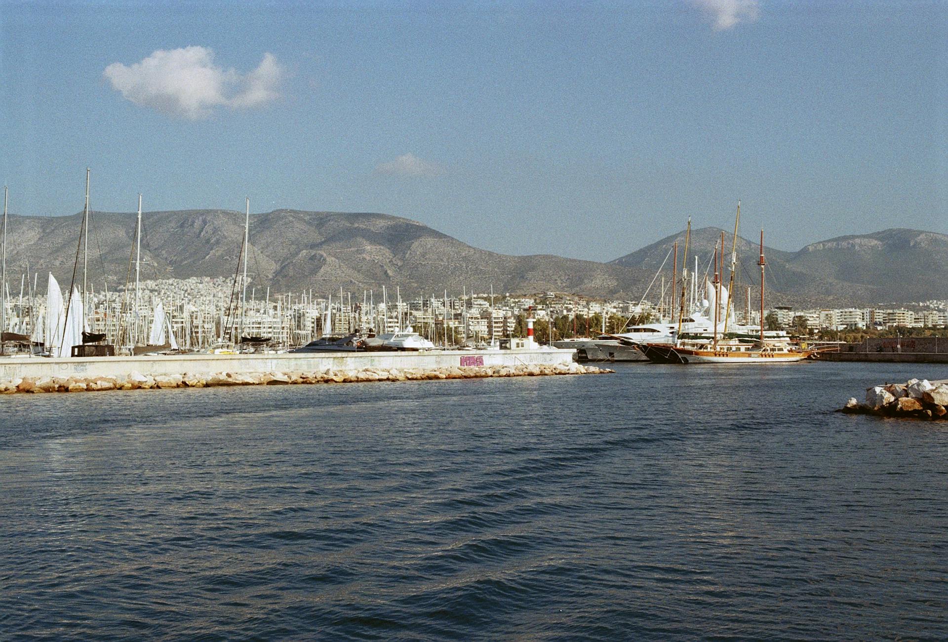 A beautiful marina scene in Athens, Greece showcasing yachts against a mountainous backdrop.