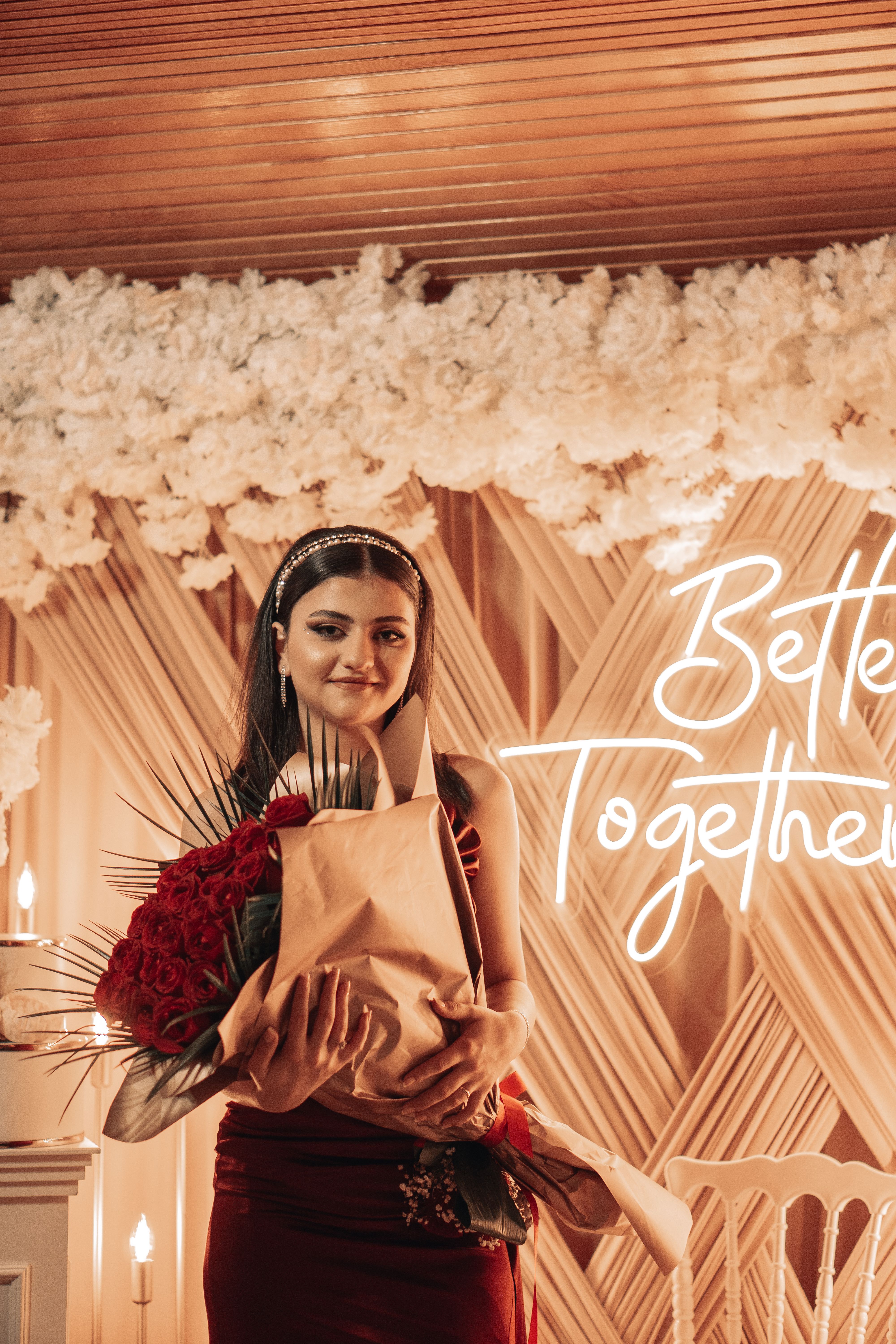 Charming woman holding flowers with elegant decor and 'Better Together' neon sign in background.