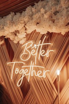 Stylish neon 'Better Together' sign with floral decor, ideal for weddings or events.