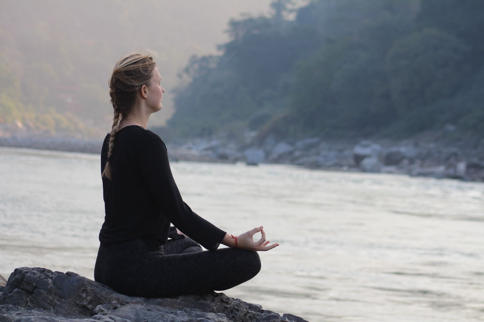 Woman meditating by a river at sunrise, reflecting the calm sattvic quality described in the gunas of yoga philosophy