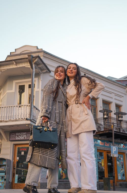 Women in Plaid and Beige Coat Standing on the Street Together