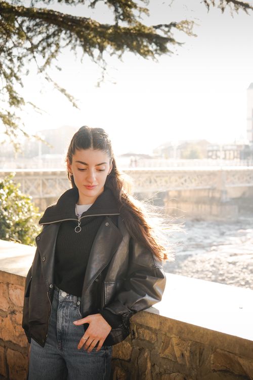 Free Stylish woman in a leather jacket poses by a riverside on a sunny day. Stock Photo