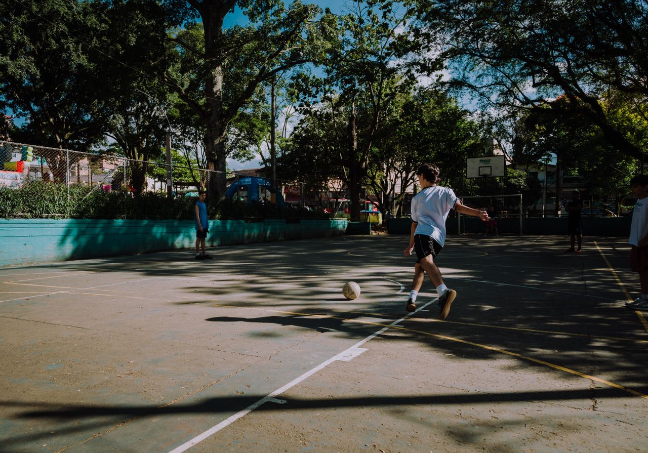 boys play a casual game of football in a sunlit park in medell n colom