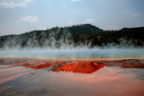 Free Majestic view of a steaming hot spring with vibrant colors and a forested backdrop. Stock Photo