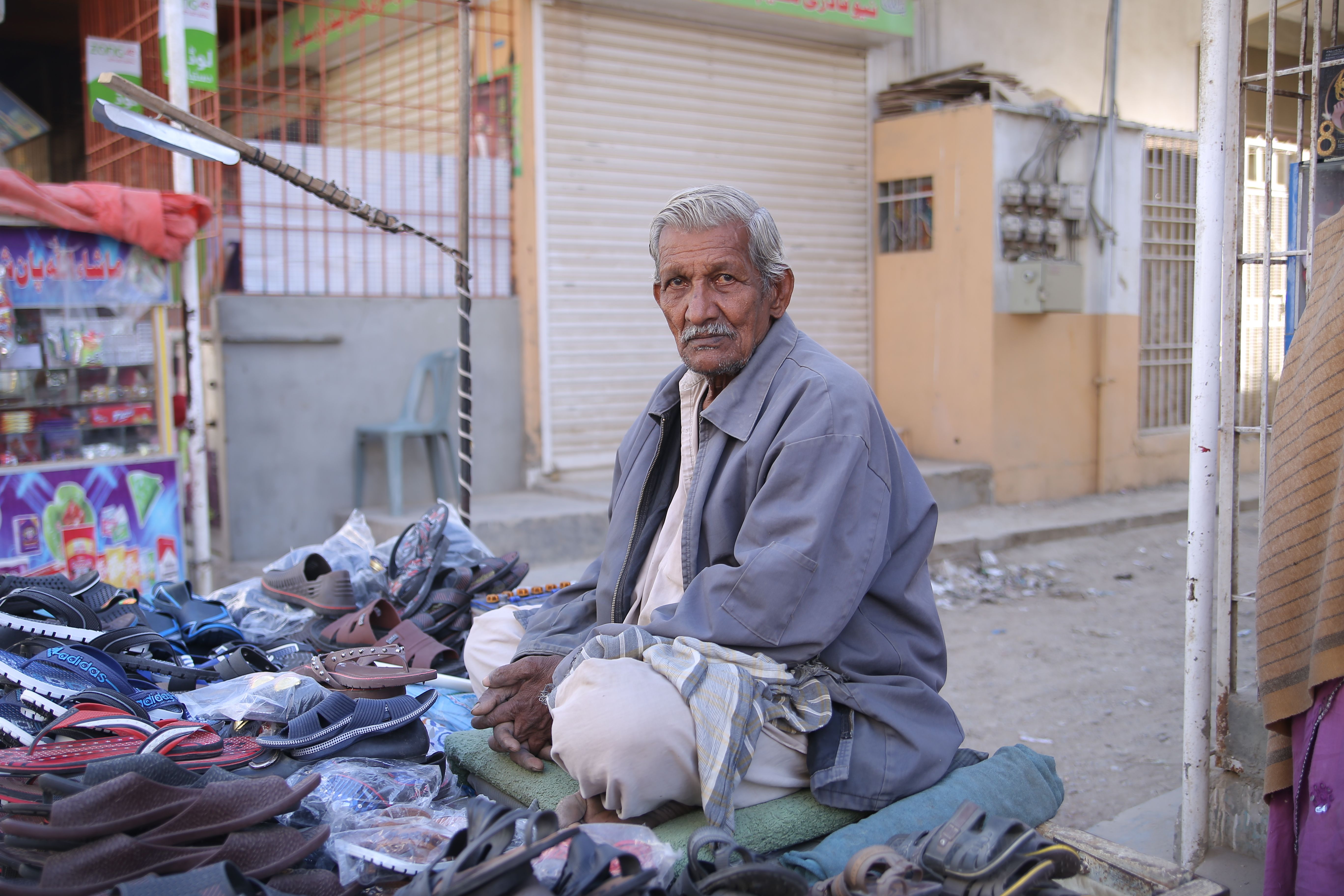 Senior man selling footwear at a street market in Karachi, Pakistan. Local commerce and lifestyle.