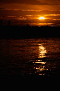 Beautiful sunset with reflection over tranquil ocean waters, creating a peaceful silhouette scene.