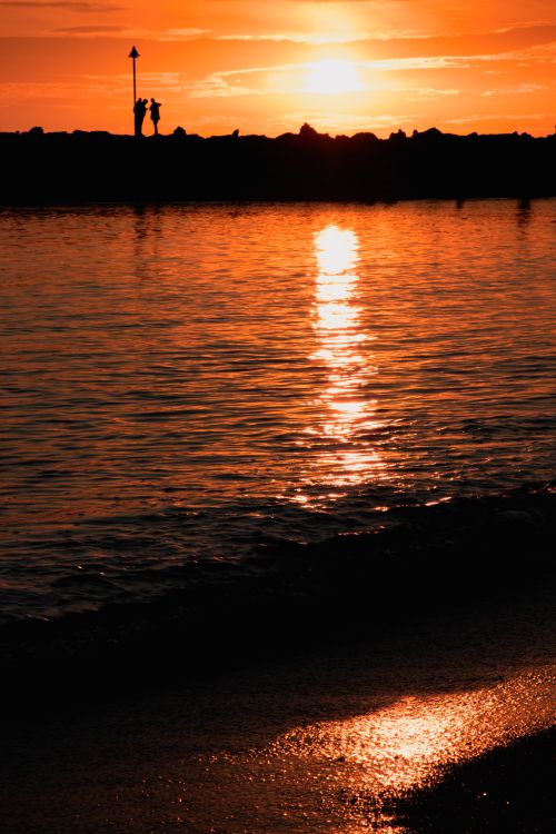 Free Silhouette of people on a promenade with a stunning sunset over the ocean. Coastal serenity. Stock Photo
