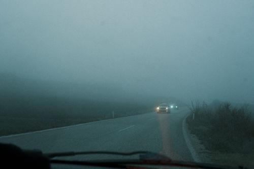 Free Cars driving on a foggy road at dawn with headlights on highlighting low visibility and atmospheric conditions. Stock Photo