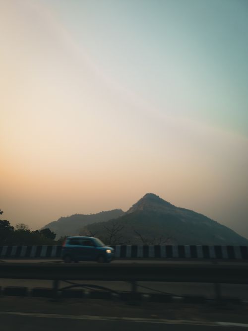 Free A car drives past a mountain during twilight, creating a dynamic landscape scene. Stock Photo