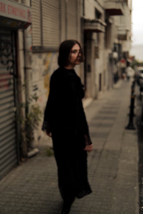A Blurry Shot of a Woman in a Black Dress Walking on a Sidewalk