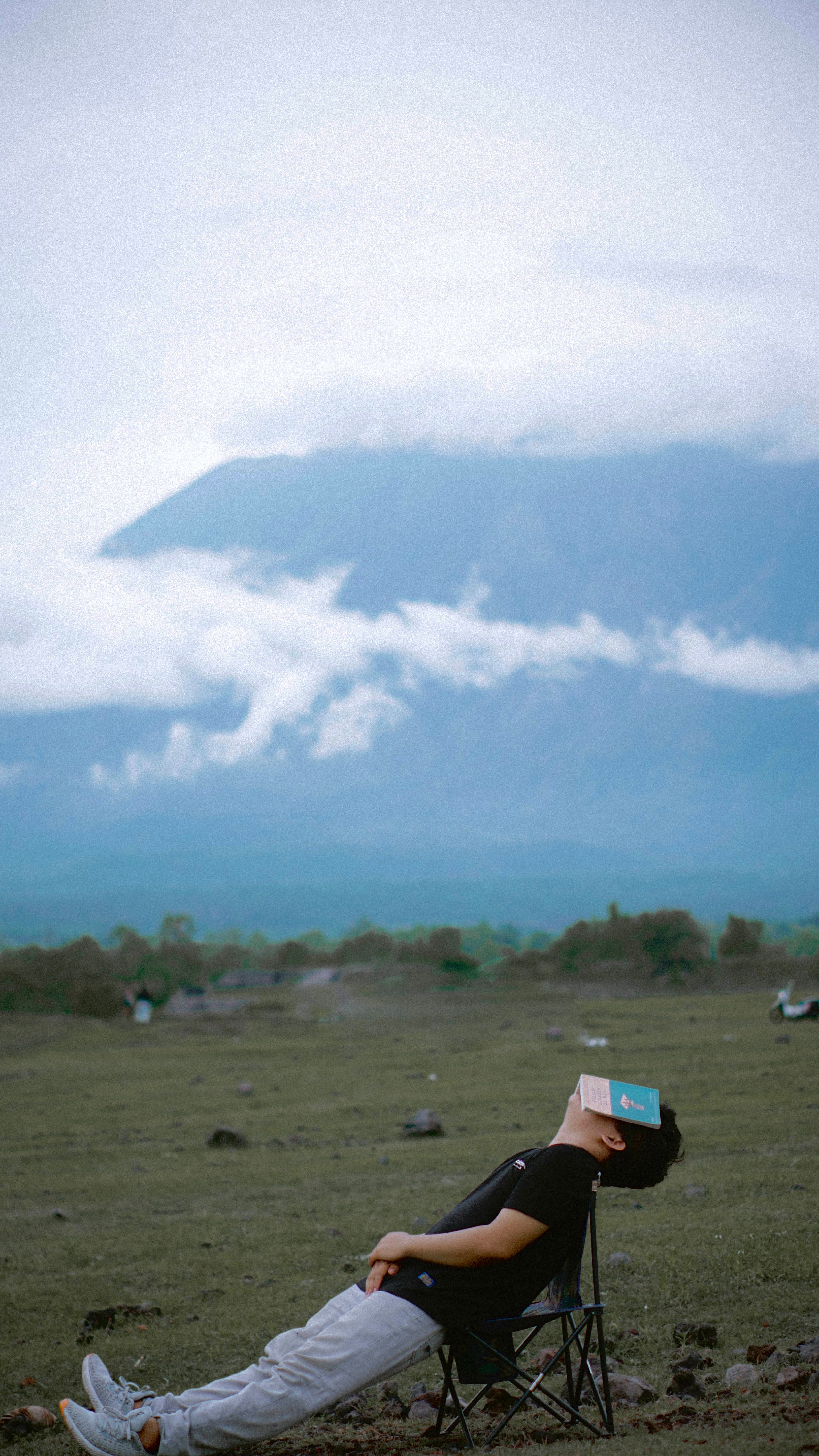 A man sits leisurely in Bali, Indonesia, reading a book with a picturesque mountain backdrop.