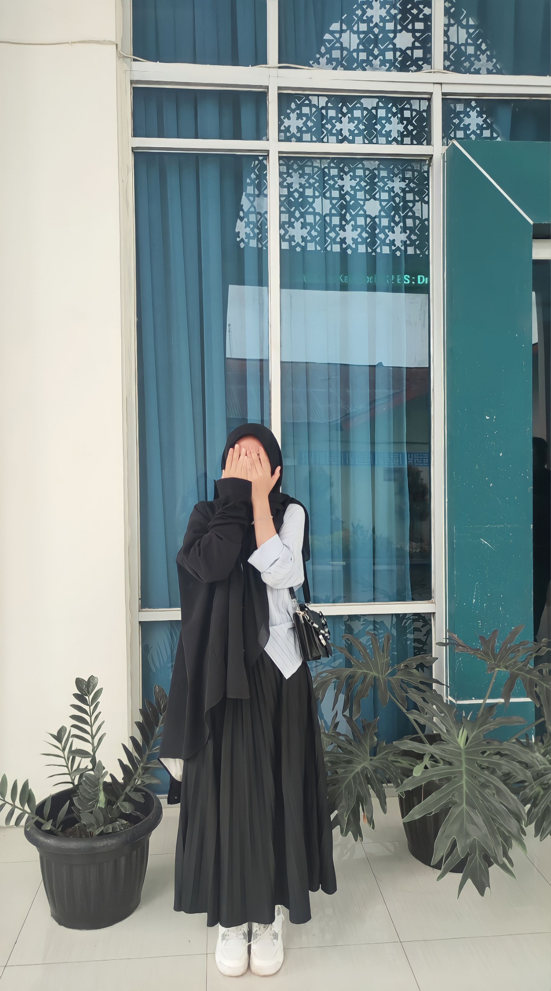 A woman playfully covers her face in front of a window in Jambi, Indonesia.
