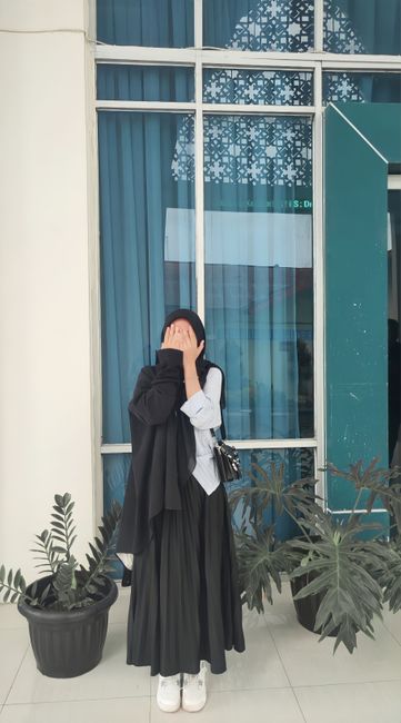 A woman playfully covers her face in front of a window in Jambi, Indonesia.