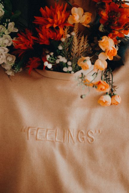 Aesthetic arrangement of vibrant flowers on a beige sweater with 'feelings' embroidered, capturing warmth and emotion.