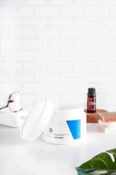 Open cosmetic cream jar on white background with natural decor.