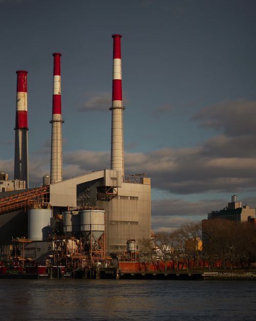 Free Dramatic view of a power plant with red chimneys by a river, under a cloudy sky. Stock Photo