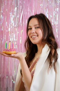 Happy woman celebrating birthday with a donut and colorful candles indoors.