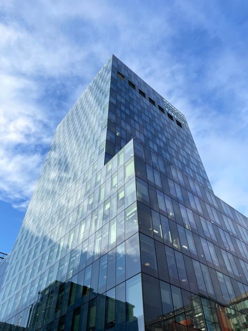 Free Contemporary glass skyscraper reflecting clouds and blue sky, showcasing modern architectural design. Stock Photo