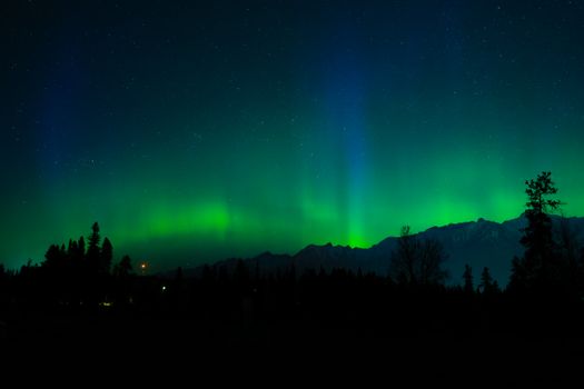 A breathtaking aurora borealis displays vibrant greens over a mountain landscape under a starry night sky.