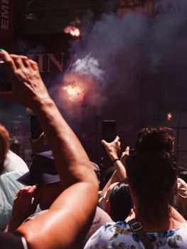 A lively crowd captures a fireworks display on smartphones during an outdoor event at night.