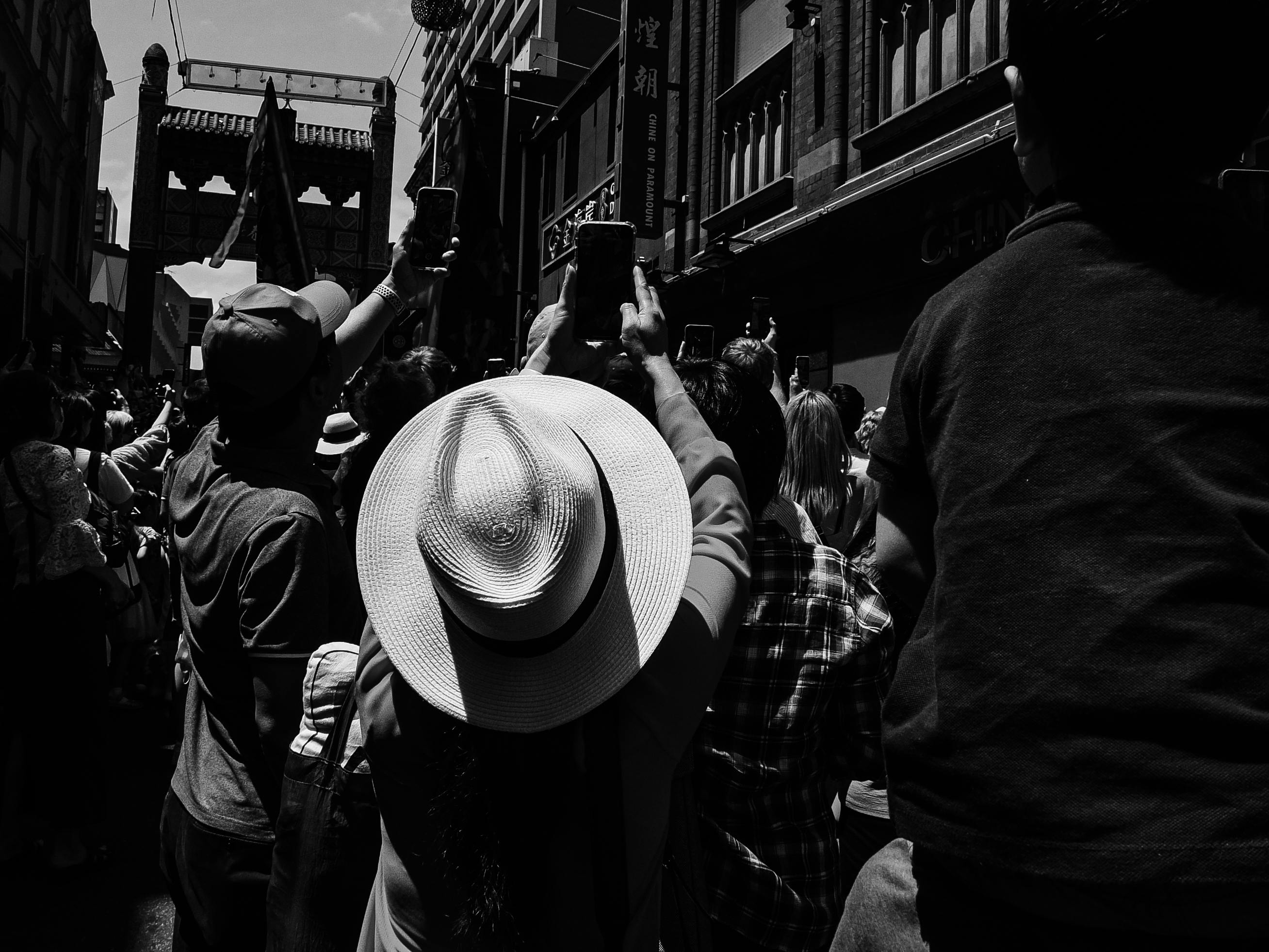 Black and white street scene with people capturing moments on their phones.
