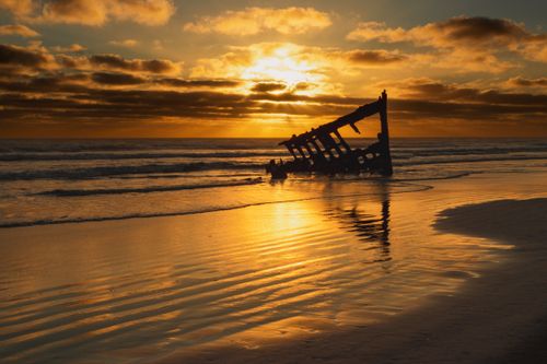 Free Beautiful sunset over a shipwreck at the beach, capturing the golden reflections in the rippling water. Stock Photo