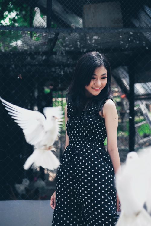 Free Young woman in polka dot dress smiling with doves flying nearby, outdoors setting. Stock Photo