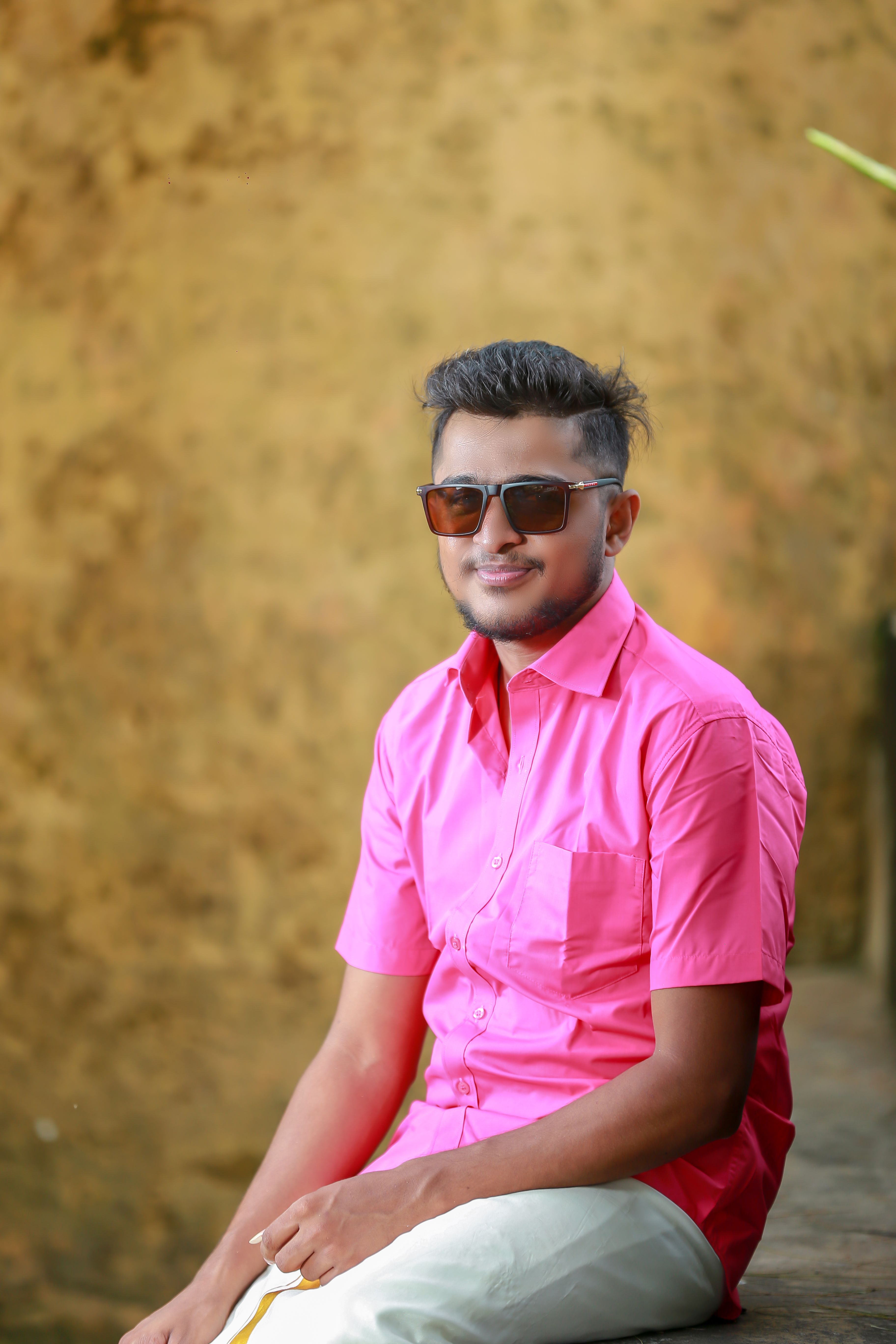 Portrait of a young man in sunglasses wearing a pink shirt, smiling outdoors.