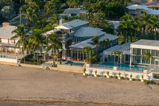 Aerial view of luxury beachfront houses with palm trees, pool, and sandy beach.