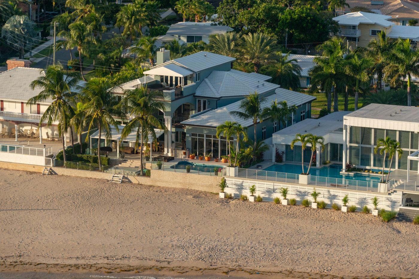 Aerial view of a beachfront resort with pool, palm trees and sandy beach