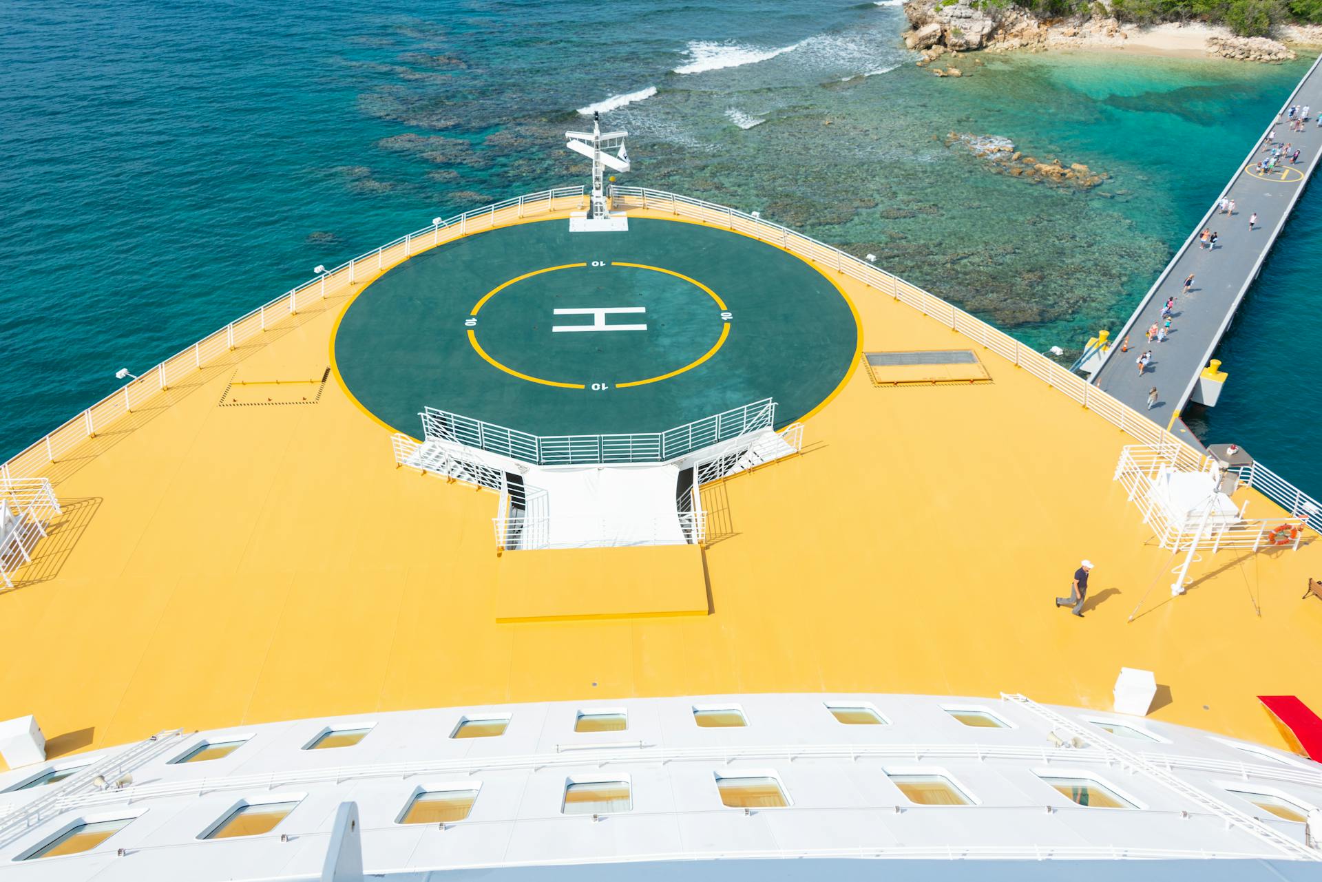 Cruise ship with a helipad docked near a tropical island with clear waters.