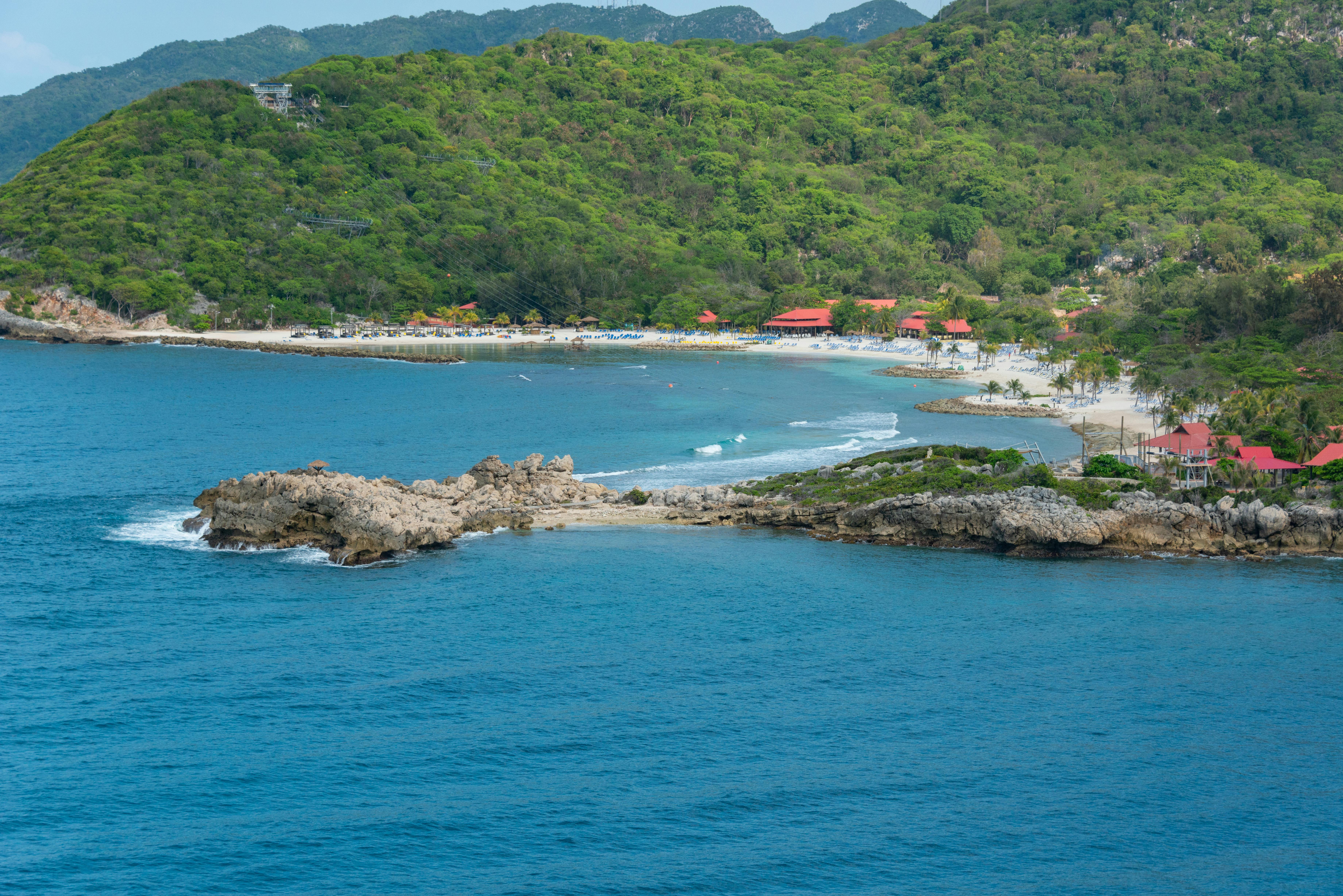 Explore a serene tropical coastline with vibrant green hills and tranquil blue waters, ideal for a summer getaway.